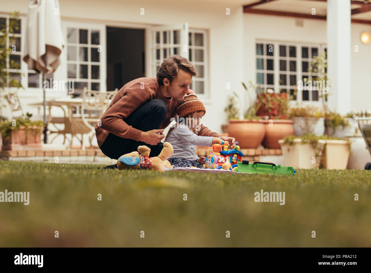 Padre e figlia seduti in giardino e giocare con i giocattoli. Padre e figlia di trascorrere del tempo insieme seduta nel loro cortile. Foto Stock