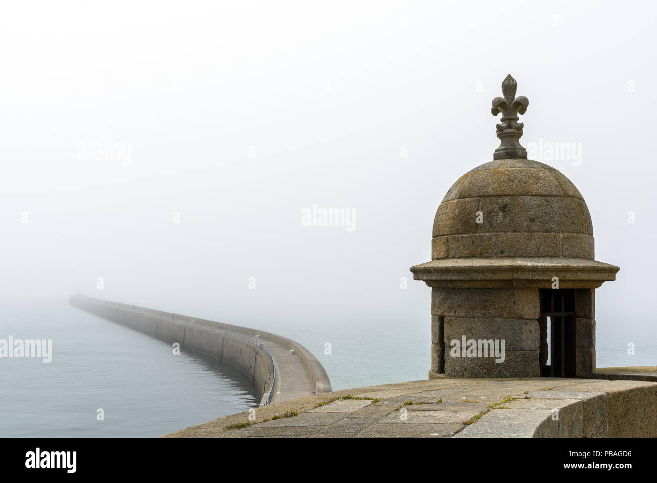 Il lungo frangiflutti delle mura di cinta della città di Saint Malo in Bretagna, Francia, visto da bastioni in foggy meteo con una torretta in primo piano. Foto Stock