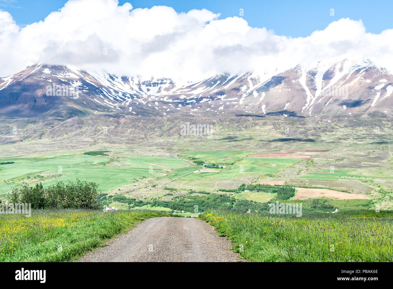 Vista sulla montagna Sulur vicino a Akureyri con cielo blu e nuvole, sporcizia strada di ghiaia, pascoli, agriturismo, ghiacciaio, neve Foto Stock