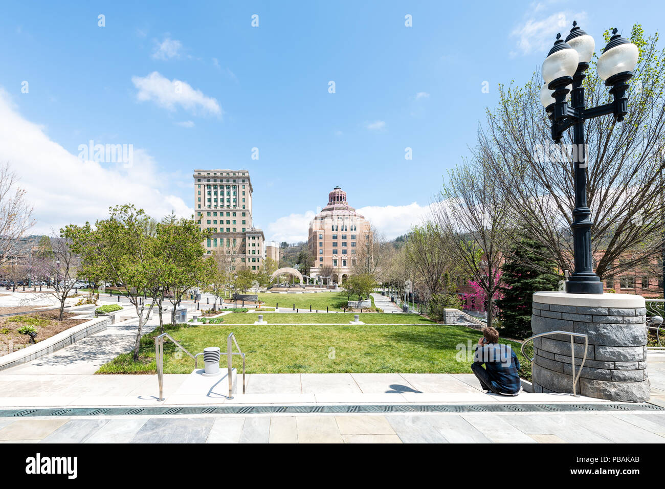 Asheville, Stati Uniti d'America - 19 Aprile 2018: Ritorno dei giovani hipster millenaria uomo seduto guardando gli edifici, courthouse e verde Pack Square Park in hippie n. Foto Stock