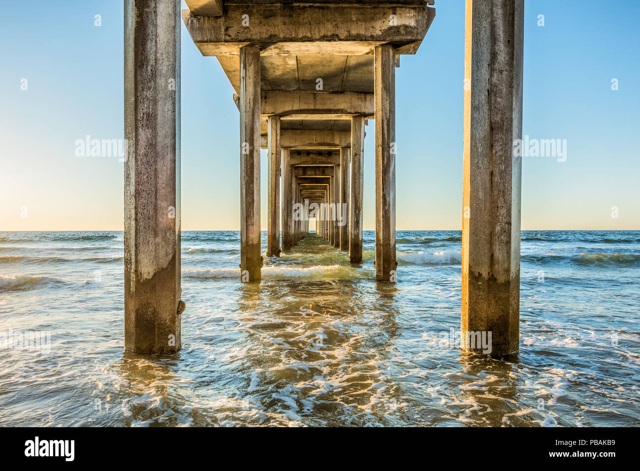 Inquadratura simmetrica sotto Scripps Pier con poli, pilastri, bel sole, sole, cielo blu, onde durante il tramonto dorato a La Jolla, San Diego, California Foto Stock