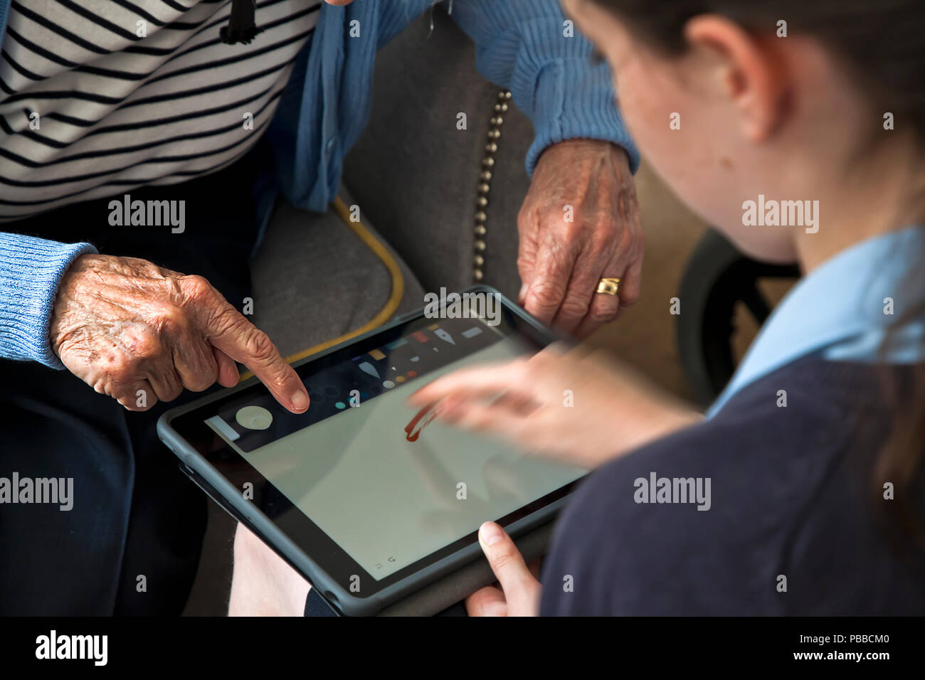 Giovani schoolgirl insegnare abilità informatiche per senior citizen su tablet sulla spalla pov Foto Stock