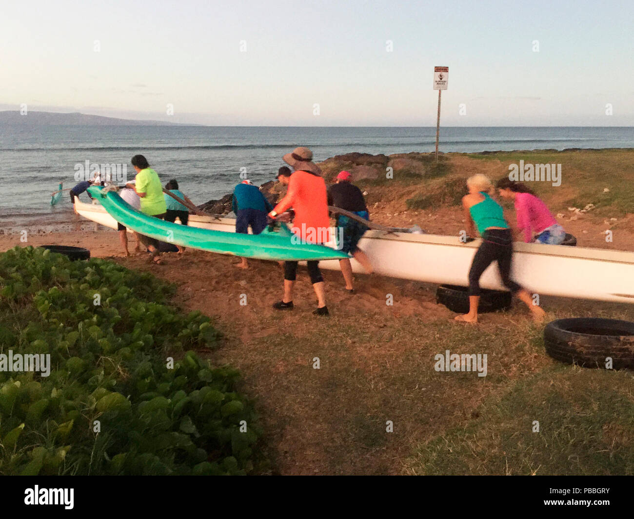 I rematori spingendo la loro barca in acqua a sunrise per un inizio di mattina pratica fila, Maui, Hawaii, STATI UNITI D'AMERICA Foto Stock