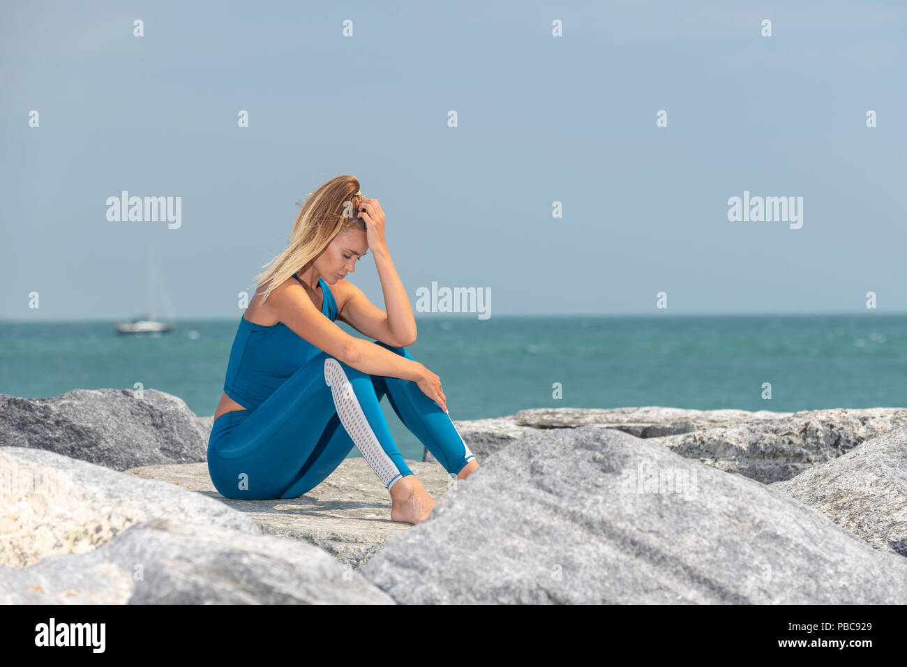 Montare sport donna esausto dopo esercizio seduti sulle rocce dal mare con la sua testa con le mani Foto Stock