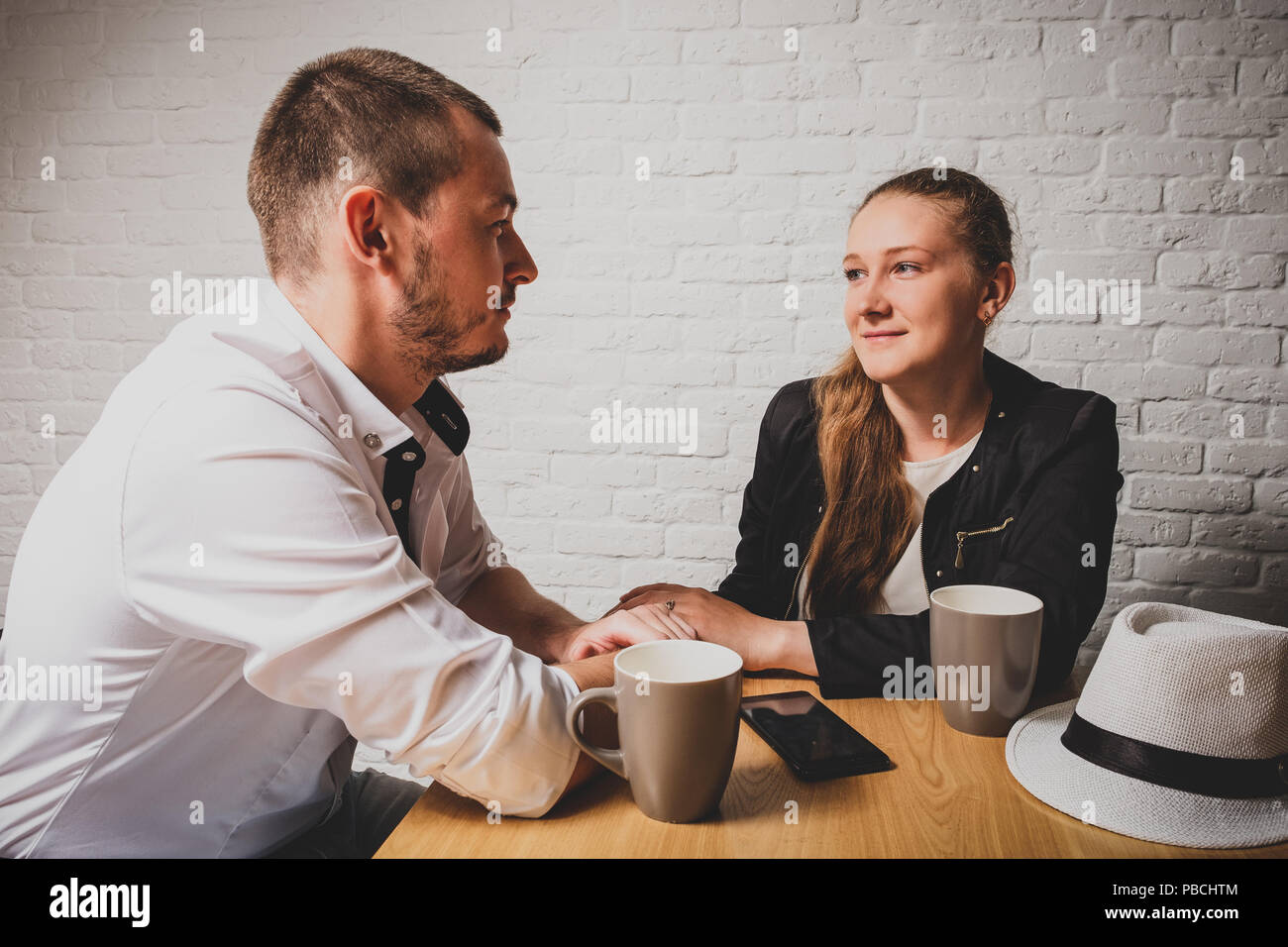 La ragazza e il ragazzo in cafe, a una tabella, parlare. Tenere le mani e guarda con amore gli uni gli altri. Su un tavolo vi è un tè, telefono e un cappello si trova a. Il ragazzo Foto Stock