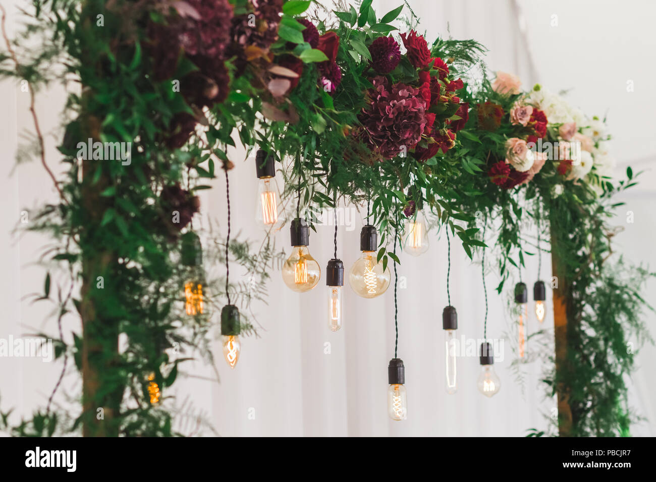 Ricevimento di nozze decorazione con vari elettrici lampade edison e rosso fresco e bordo fiori, stile rustico Foto Stock