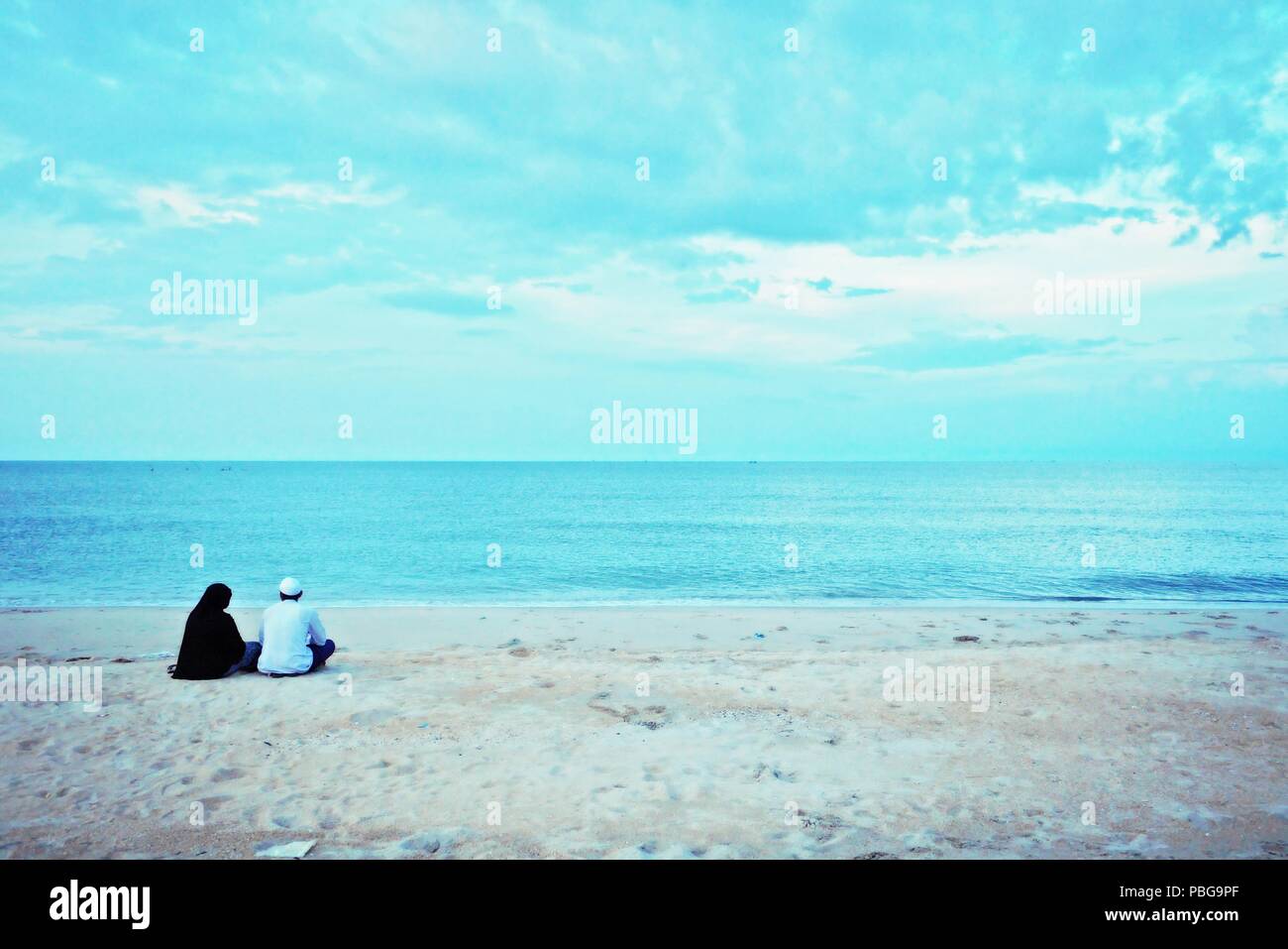 Il retro dei musulmani l uomo e la donna seduta insieme sulla spiaggia, guardando avanti al mare. Turismo Halal del giovane musulmano con seascape sfondo. Foto Stock