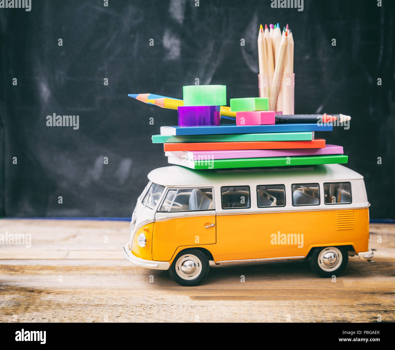 Si torna a scuola concetto. Forniture scolastiche e scuola bus sulla scrivania in legno, sfondo blackboard Foto Stock