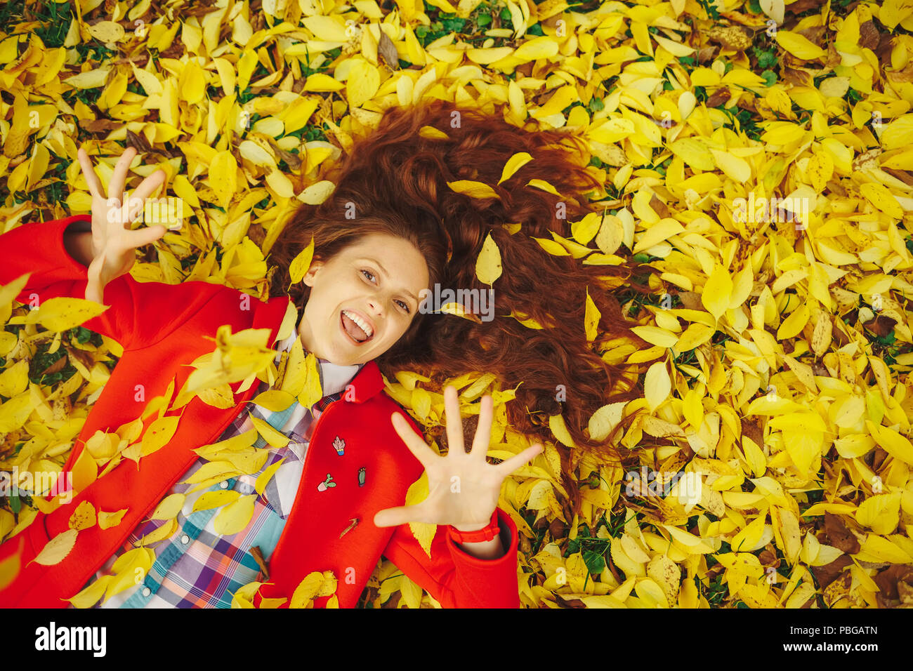 Bella ragazza felice che stabilisce in giallo le foglie di autunno. Foto Stock