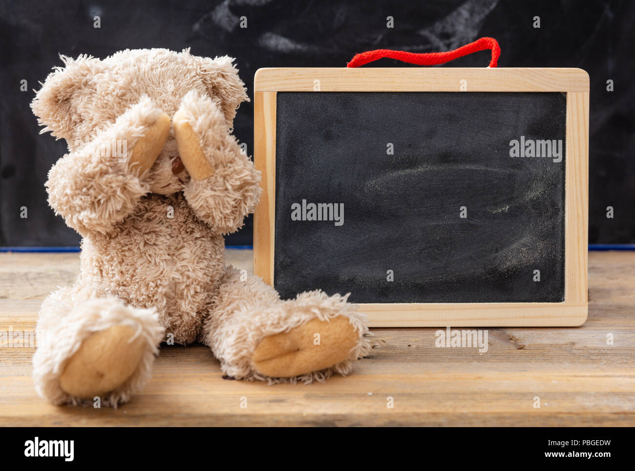 Il bullismo a scuola o difficoltà di apprendimento del concetto. Orsacchiotto di peluche che copre gli occhi e una lavagna vuota, lo spazio per il testo Foto Stock