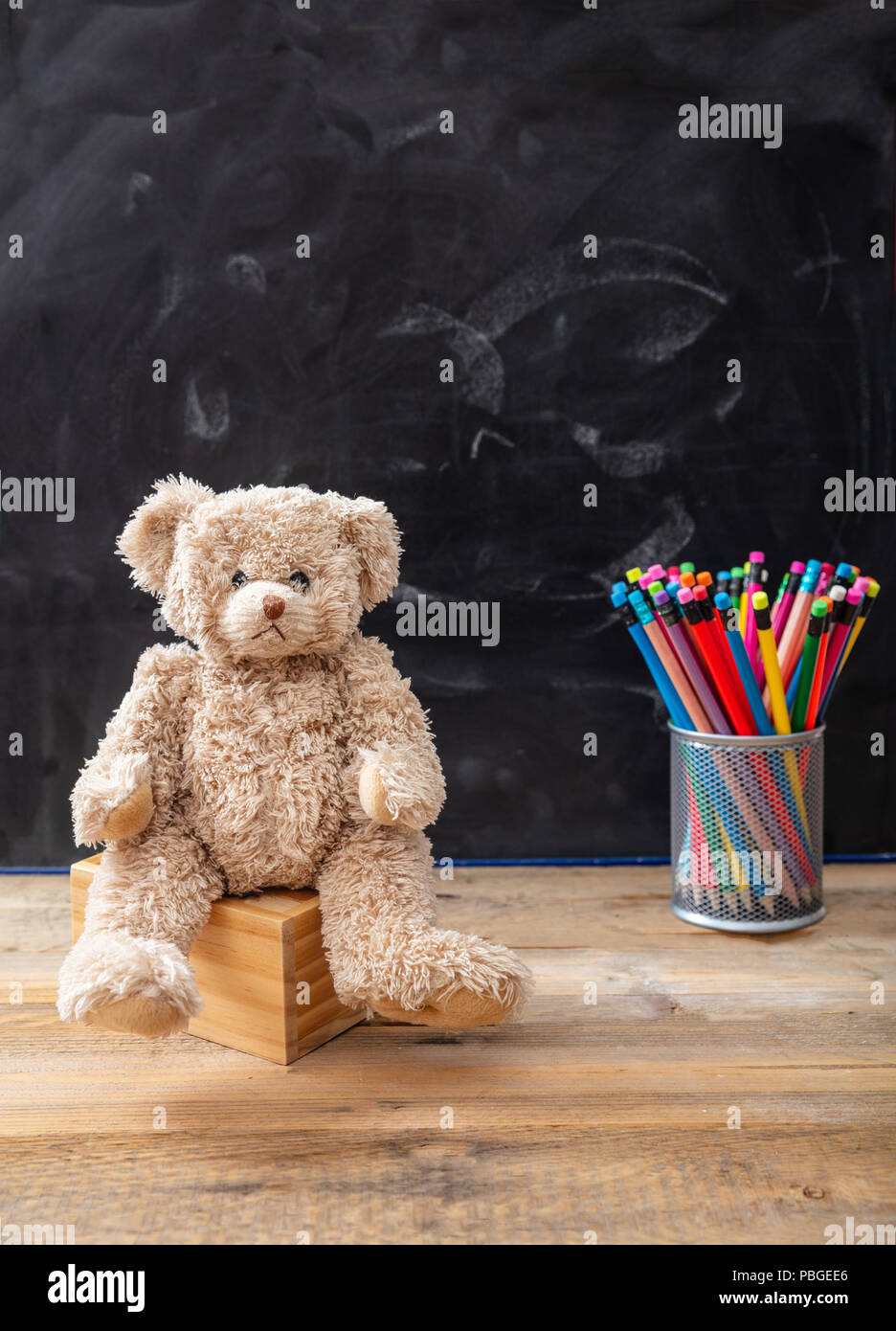 Si torna a scuola. Orsacchiotto di peluche e matite colorate su sfondo blackboard, spazio di copia Foto Stock