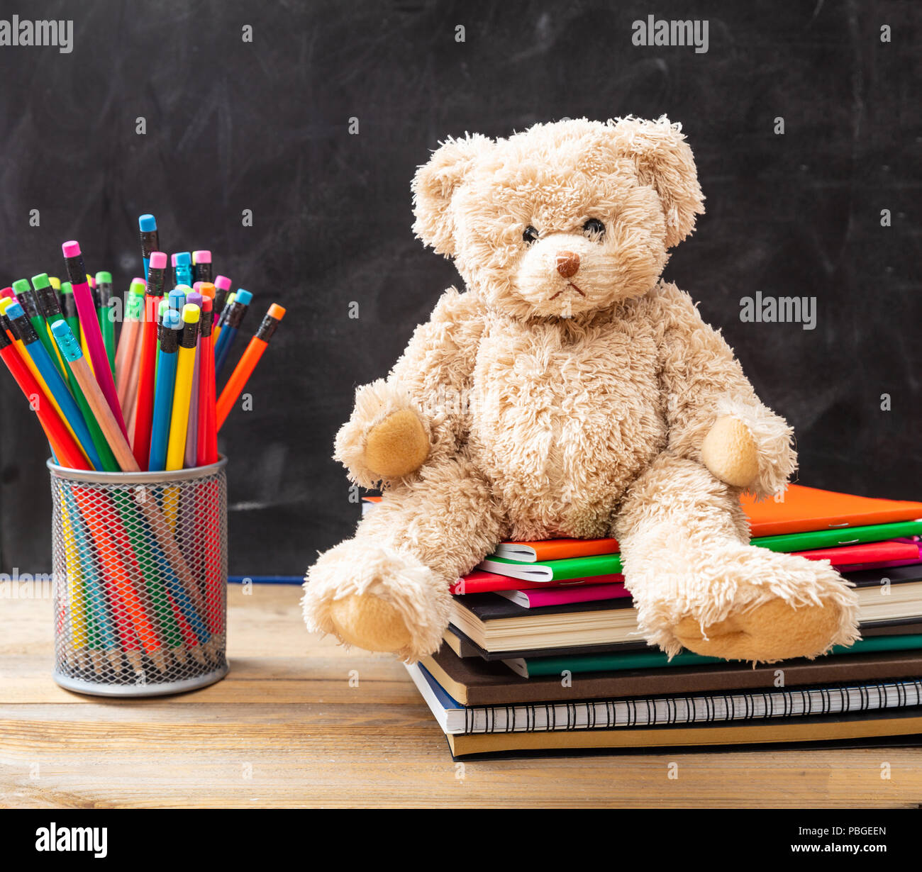 Si torna a scuola. Orsacchiotto di peluche e matite colorate e quaderni di sfondo blackboard Foto Stock