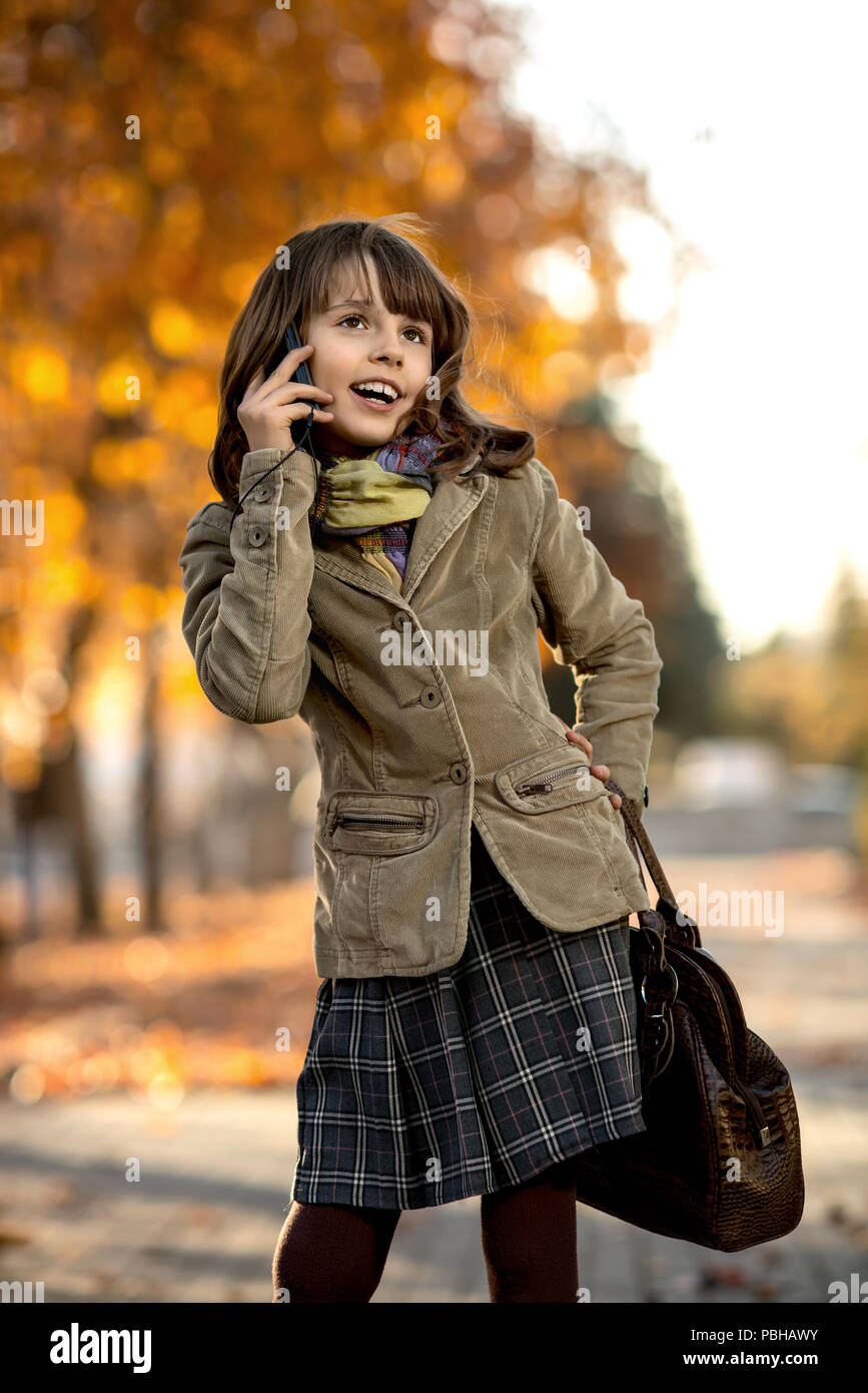 Foto verticale, elegante bella bambina tenere il telefono cellulare e la gioia di parlare Foto Stock
