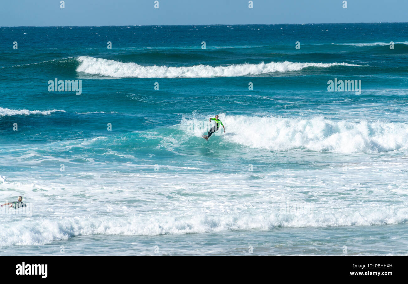 COOLANGATTA, Australia - luglio10 2018; ampia spiaggia per il surf con surfer cavalcando attraverso onda bianco schiuma con profondo mare turchese dietro Foto Stock