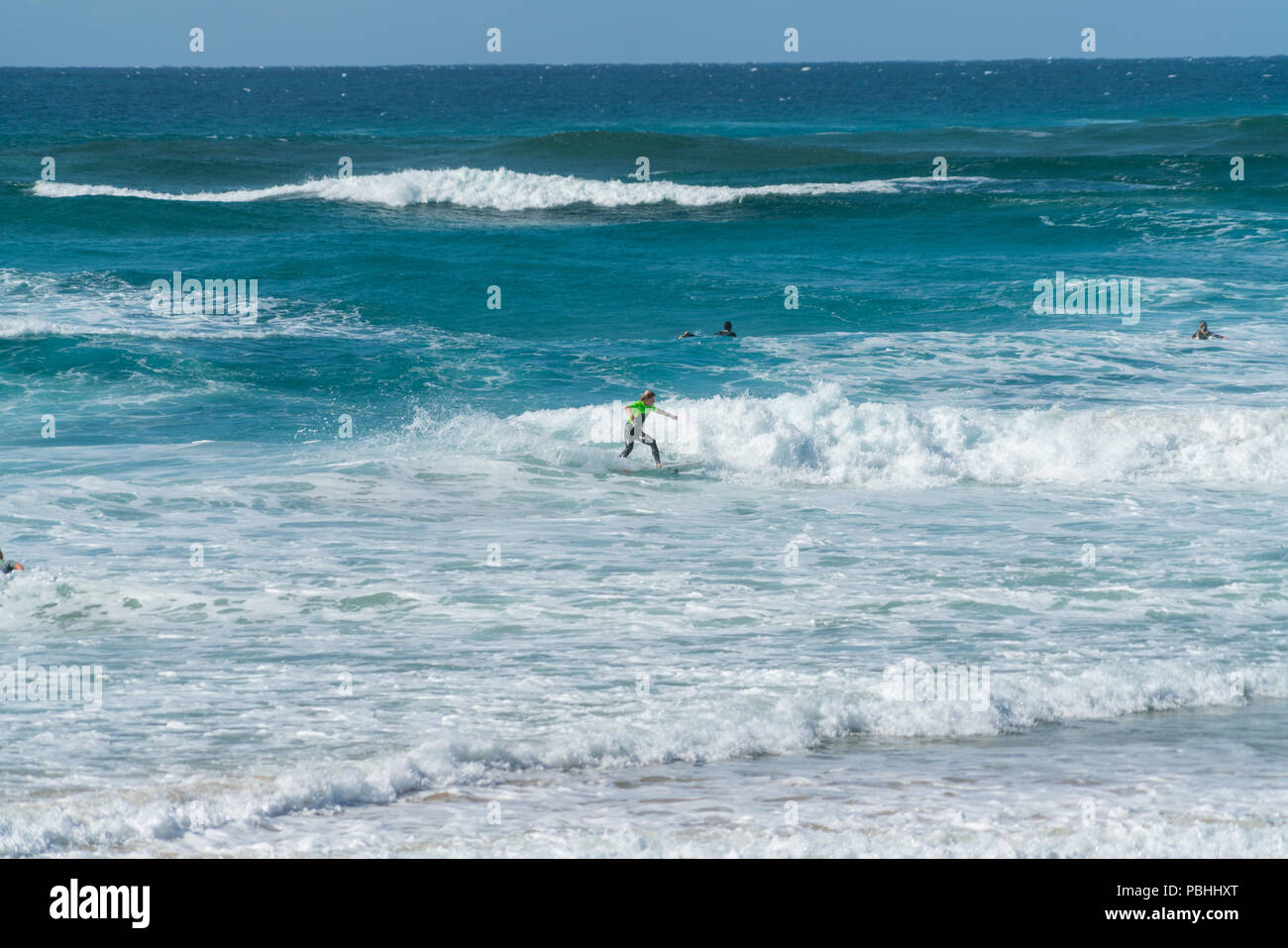 COOLANGATTA, Australia - luglio10 2018; ampia spiaggia per il surf con surfer cavalcando attraverso onda bianco schiuma con profondo mare turchese dietro Foto Stock