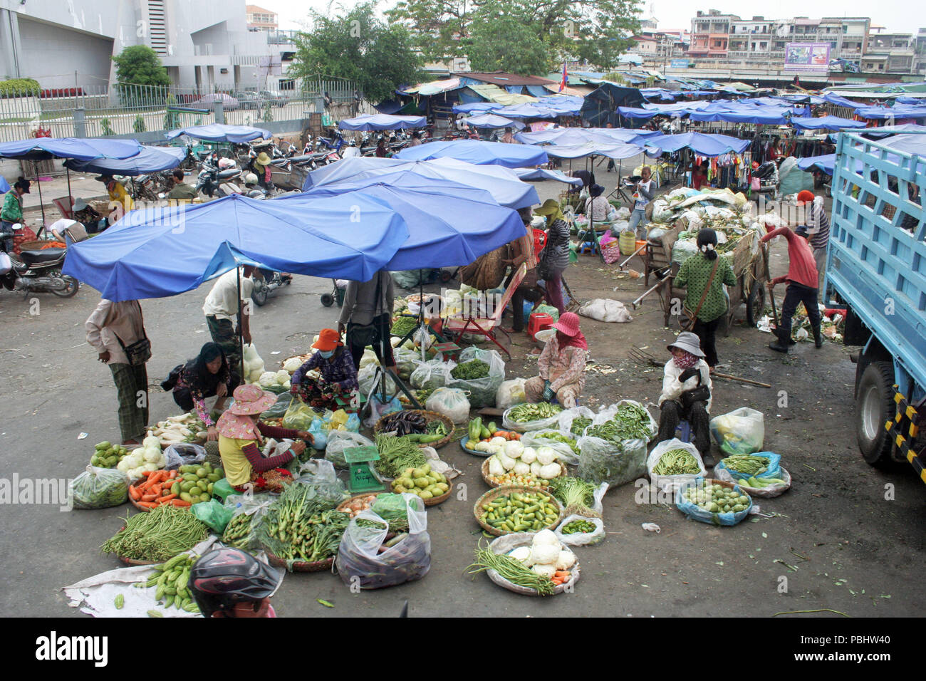 Mercato occupato sotto ombrelloni blu con edifici in background, Cambogia Foto Stock