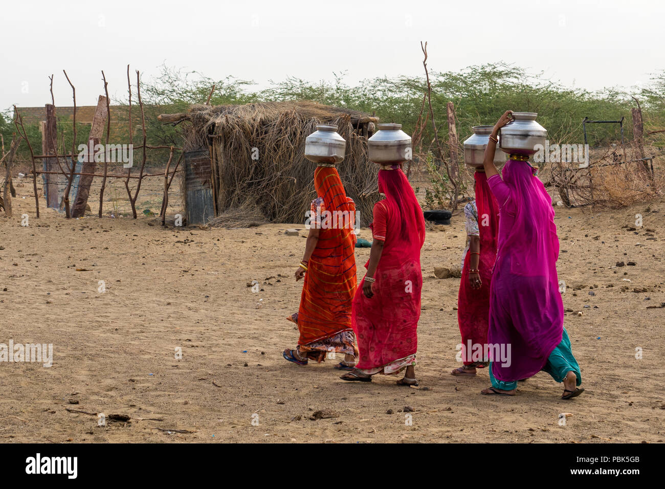 Le donne delle zone rurali portano caraffe di metallo con acqua sulle loro teste. Deserto Parco Nazionale di Jaisalmer India Giugno 2018 Foto Stock