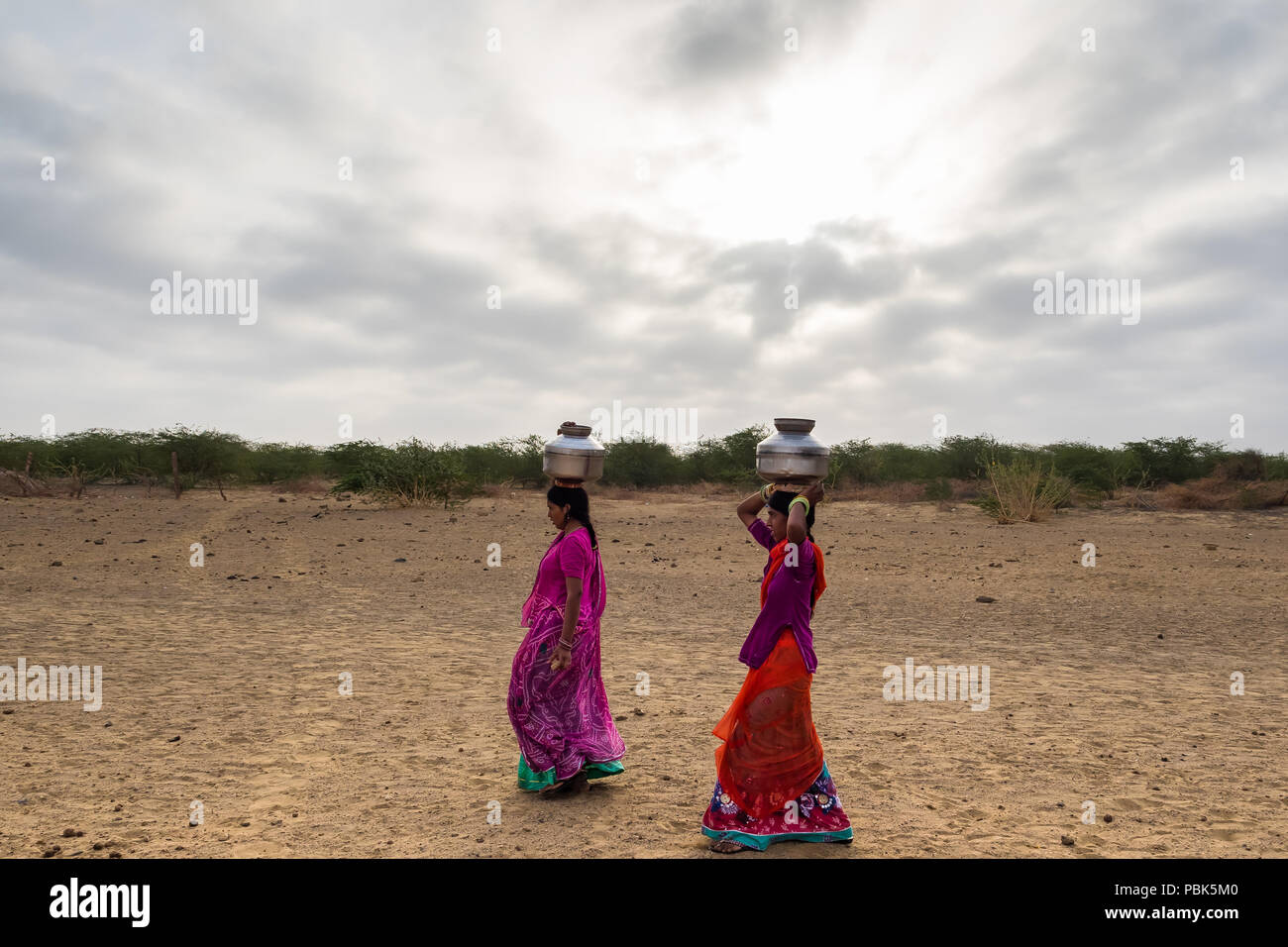 Le donne delle zone rurali portano caraffe di metallo con acqua sulle loro teste. Deserto Parco Nazionale di Jaisalmer India Giugno 2018 Foto Stock