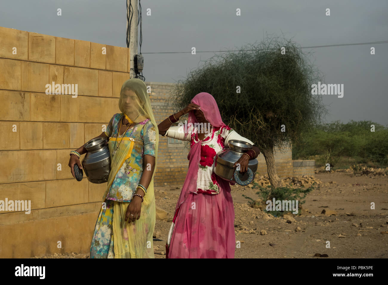 Le donne delle zone rurali portano caraffe di metallo con acqua sulle loro teste. Deserto Parco Nazionale di Jaisalmer India Giugno 2018 Foto Stock
