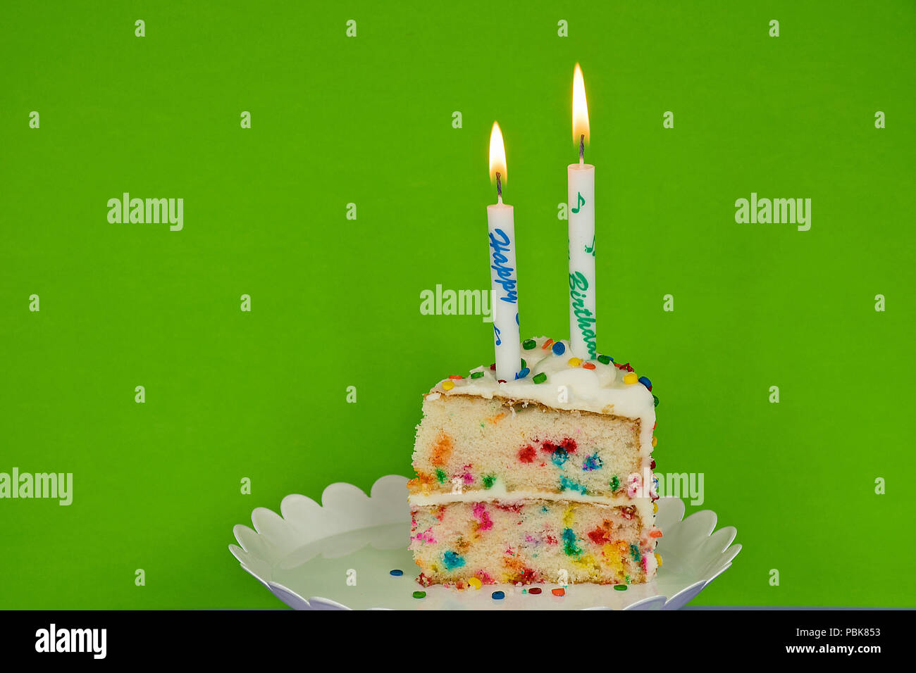 Fetta di torta di compleanno con candele su neon sfondo verde Foto Stock