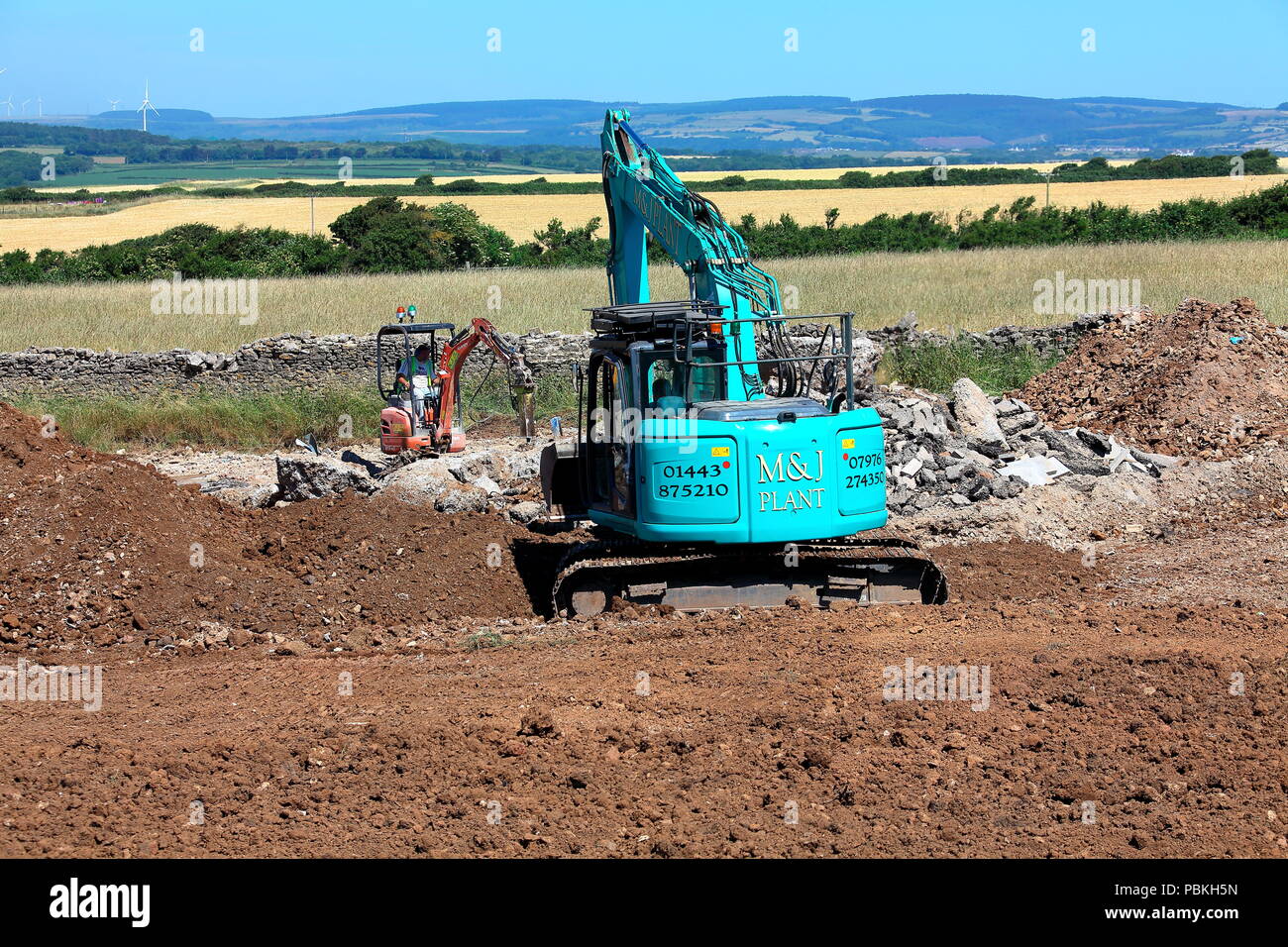 Grandi e piccoli in macchinari di impianto mondo, due escavatori a lavorare in un campo in fase di ripristino di terreni agricoli dopo il completamento dei lavori di costruzione. Foto Stock