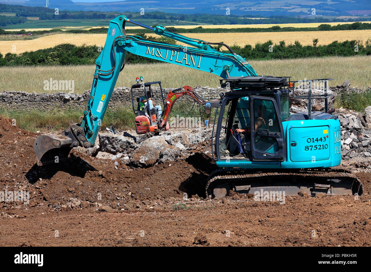Grandi e piccoli in macchinari di impianto mondo, due escavatori a lavorare in un campo in fase di ripristino di terreni agricoli dopo il completamento dei lavori di costruzione. Foto Stock
