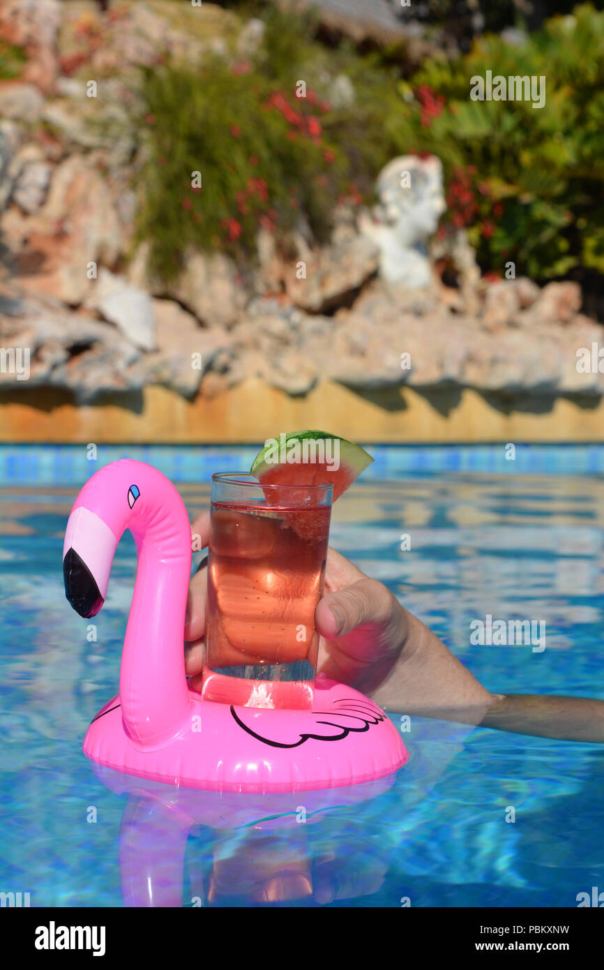 Donna di mano , con un cocktail in un gonfiabile fenicottero rosa floating portabicchiere in una piscina. Estate vibes! Foto Stock