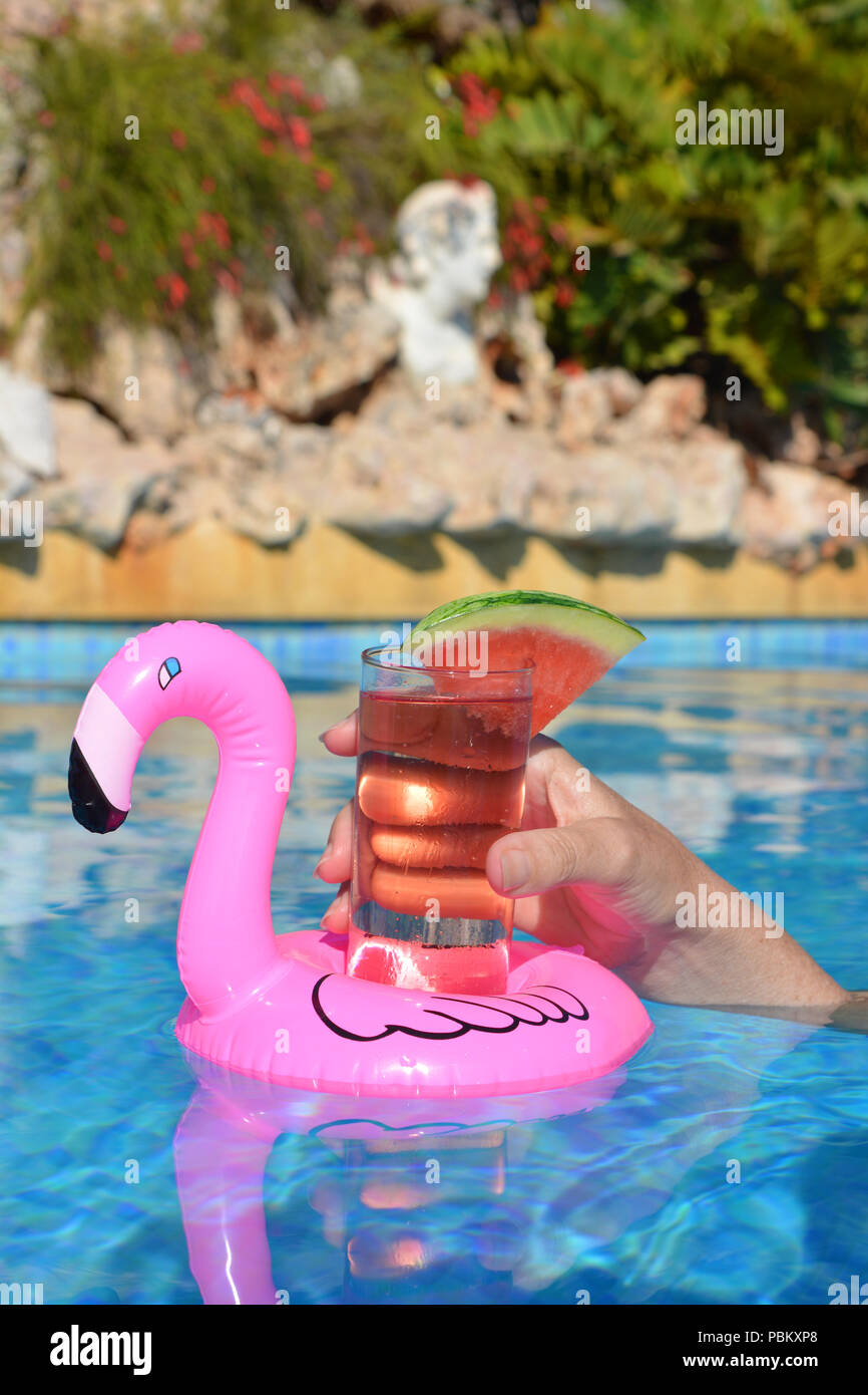 Donna di mano , con un cocktail in un gonfiabile fenicottero rosa floating portabicchiere in una piscina. Estate vibes! Foto Stock