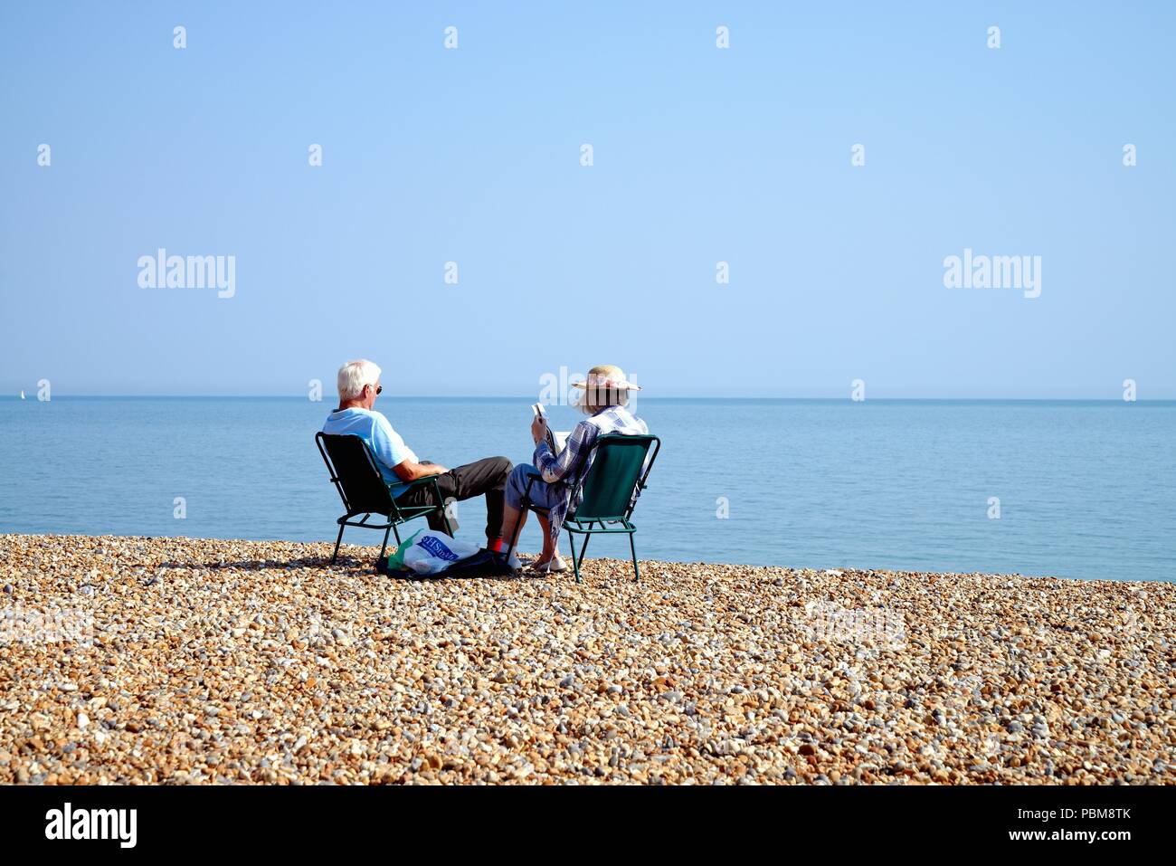 Anziana coppia bianco seduto sulla spiaggia a Hastings in una calda giornata estiva, East Sussex England Regno Unito Foto Stock
