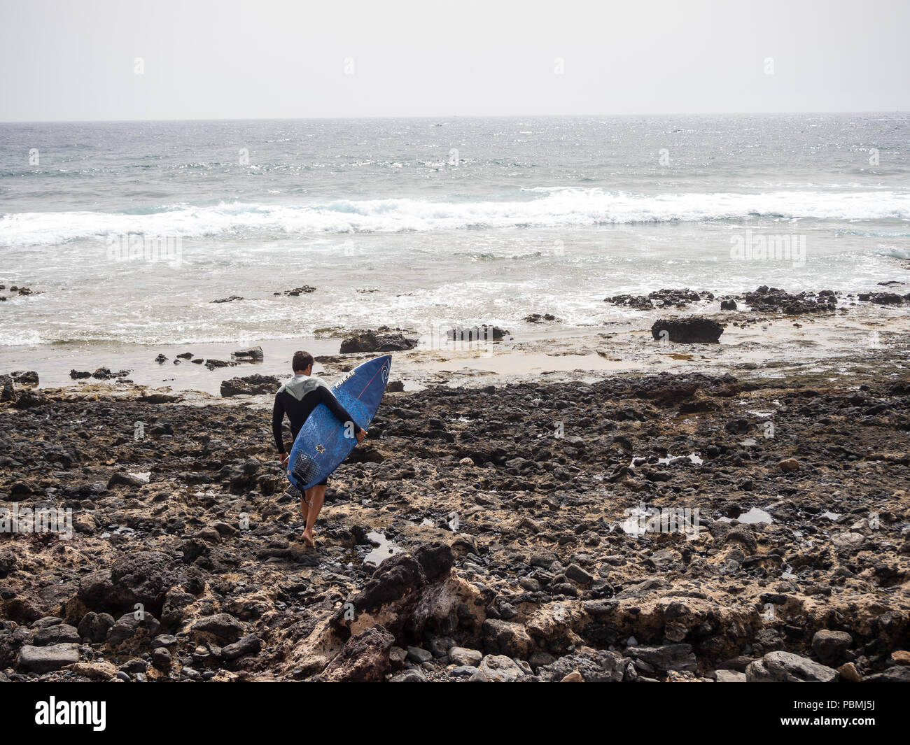 Playa de Las Americas, Tenerife, Spagna - 10 Luglio 2018: Surfer attraversando a piedi sulle rocce verso il mare sulla spiaggia di Las Americas Foto Stock