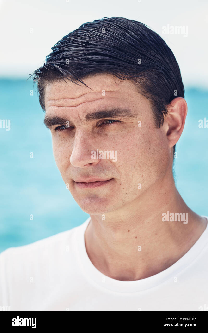 Close-up verticale di uno bianco uomo caucasico con scuri piccoli occhi e capelli corti che guarda lontano fuori dall'acqua mare sulla spiaggia Foto Stock