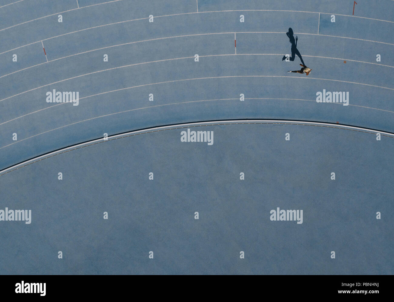 Sprinter in esecuzione sulla pista di atletica leggera. Vista dall'alto di un velocista in esecuzione su pista in uno stadio con ombra che cade sul lato. Foto Stock