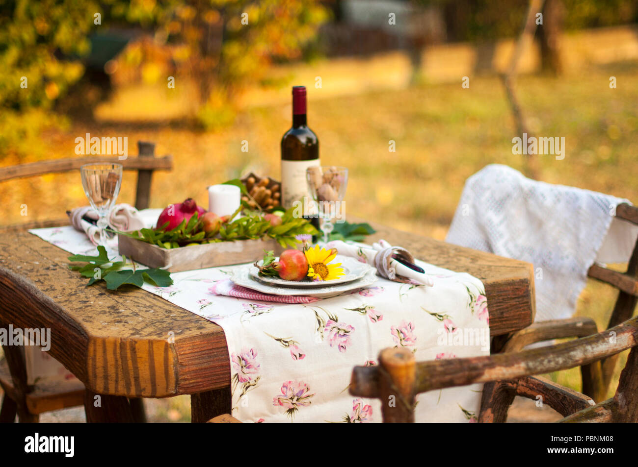 Cena romantica a lume di candela nel giardino d'autunno, impostazione tabella per una bella cena. Vino, frutta, melograno e fiori. Pic-nic all'aria aperta Foto Stock