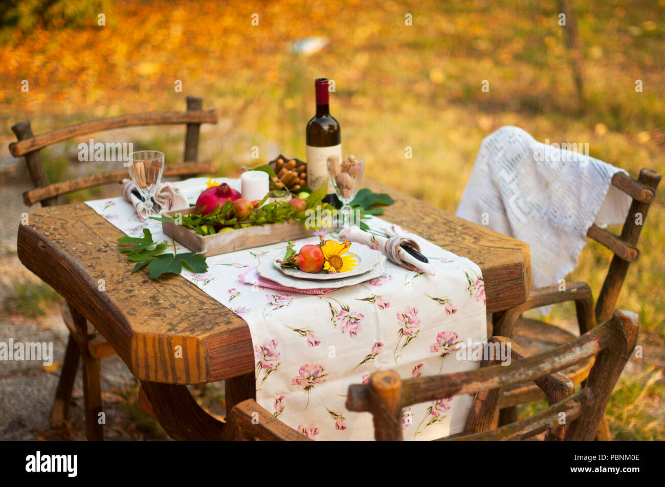 Cena romantica a lume di candela nel giardino d'autunno, impostazione tabella per una bella cena. Vino, frutta, melograno e fiori. Pic-nic all'aria aperta Foto Stock