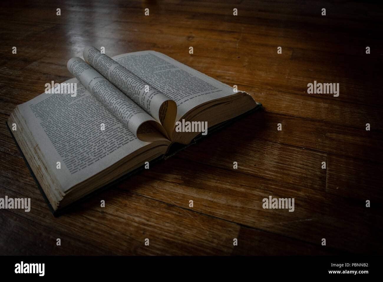 Libro aperto su di un pavimento in legno con heartshaped aprire le pagine al centro e un po' di luce naturale. Foto Stock