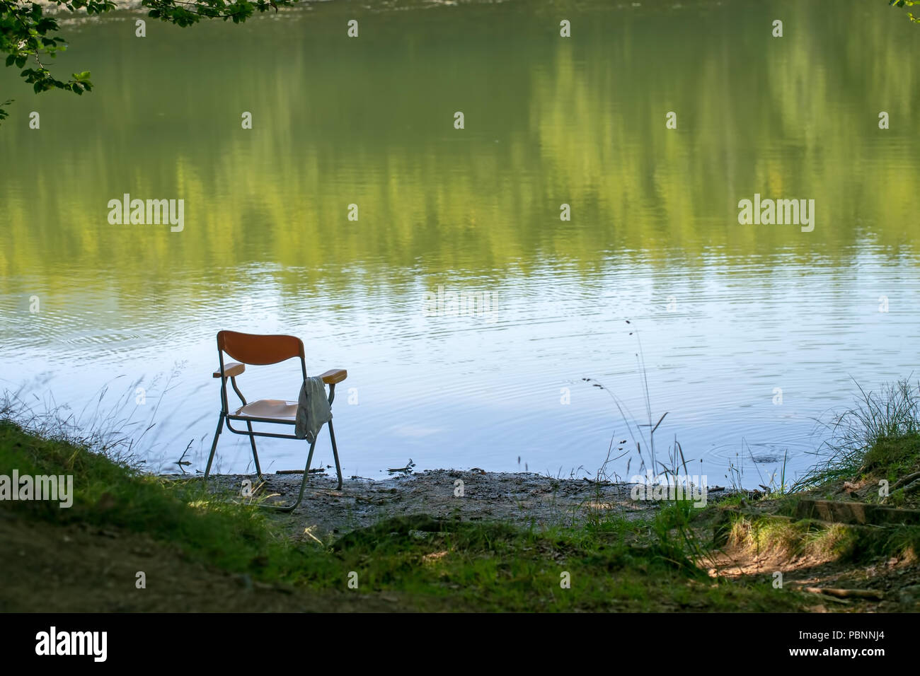 Andando a pesca, forse, sedia a sinistra dal bordo del lago. L'estate. Sfondo, nessuno in sede sul lago. Foto Stock