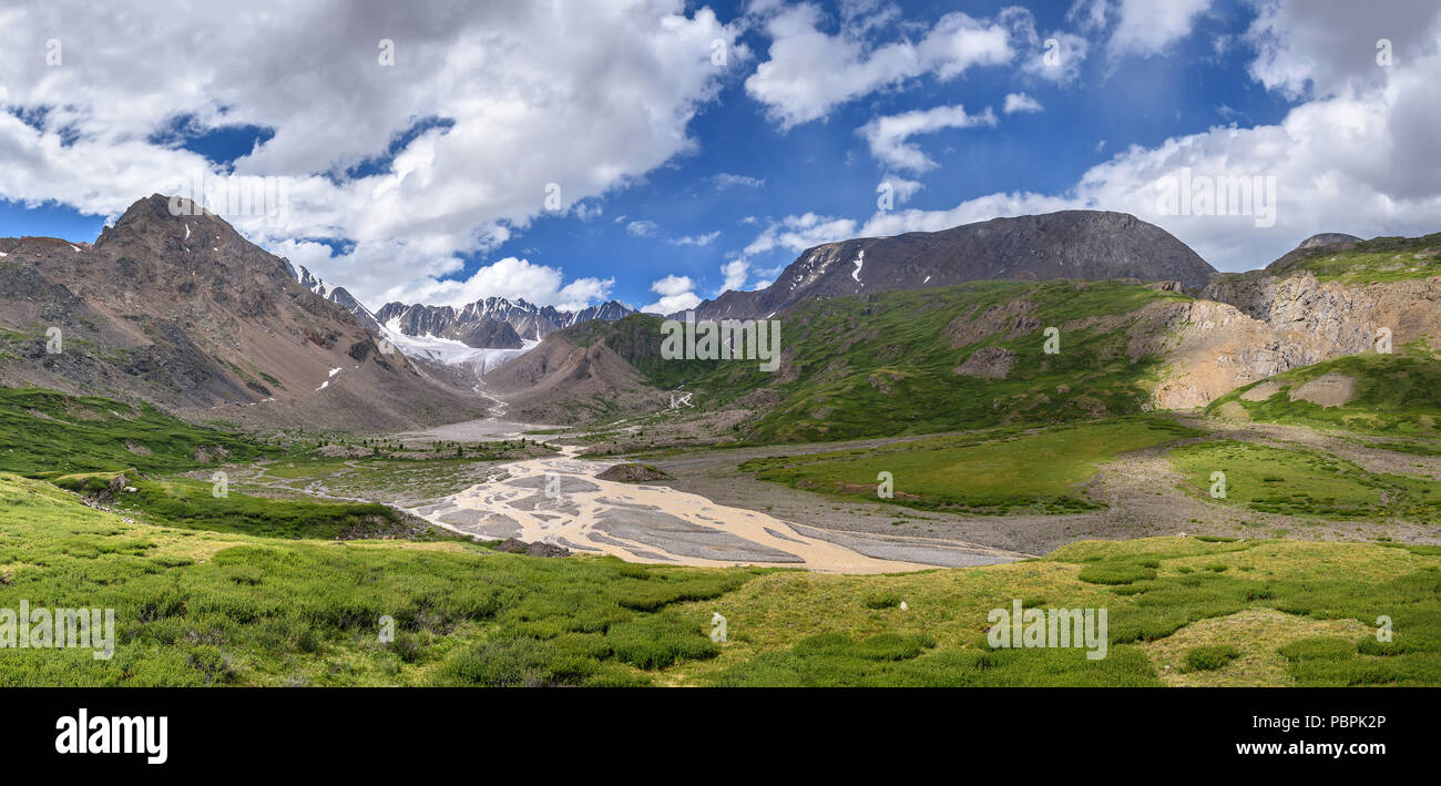 Un fantastico panorama con un bellissimo ghiacciaio in montagna, una verde vallata con un fiume, una boccola e pietre contro uno sfondo di cielo blu e nuvole Foto Stock