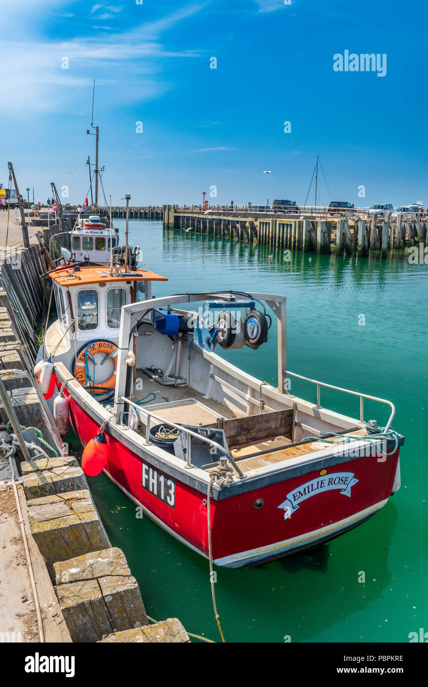 Una piccola barca da pesca attende presso il molo di attracco per scaricare la sua cattura la aqua acque verdi di West Bay nel Dorset. Foto Stock