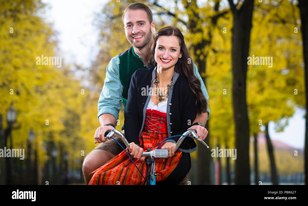 Matura in Dirndl e pantaloni in pelle insieme su una bicicletta Foto Stock