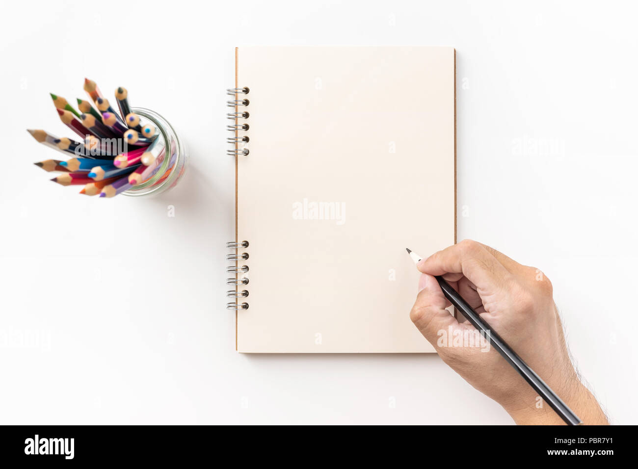 Concetto di Design - vista superiore della spirale kraft notebook, pagina vuota, portapenna e mano d'uomo tenendo la penna a colori isolati su sfondo bianco per mockup Foto Stock
