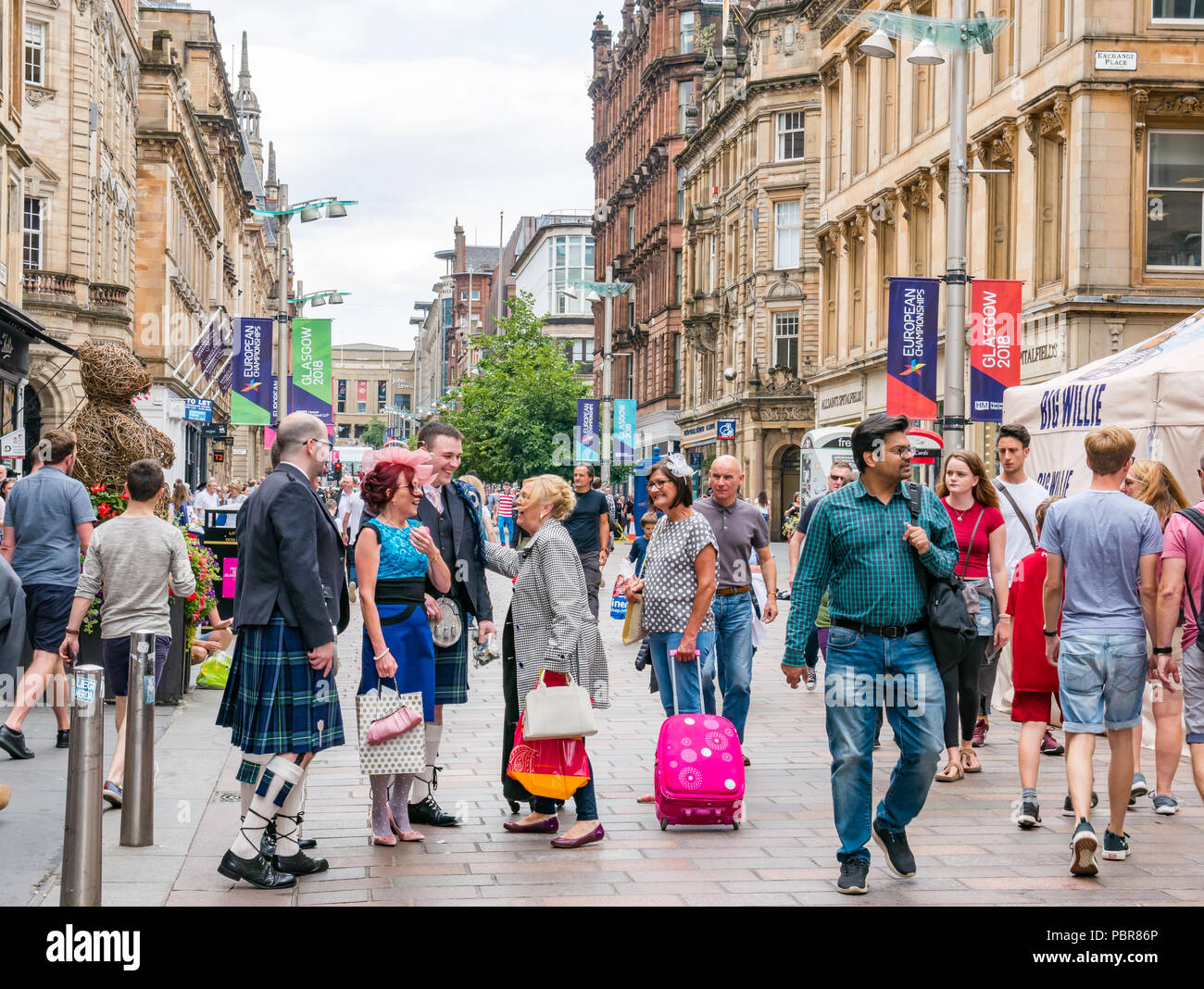 Persone vestite per un matrimonio con uomini in kilts fermarsi per dire ciao e saluto ciascuno di altri in una strada trafficata, Buchanan Street, Glasgow, Scotland, Regno Unito Foto Stock