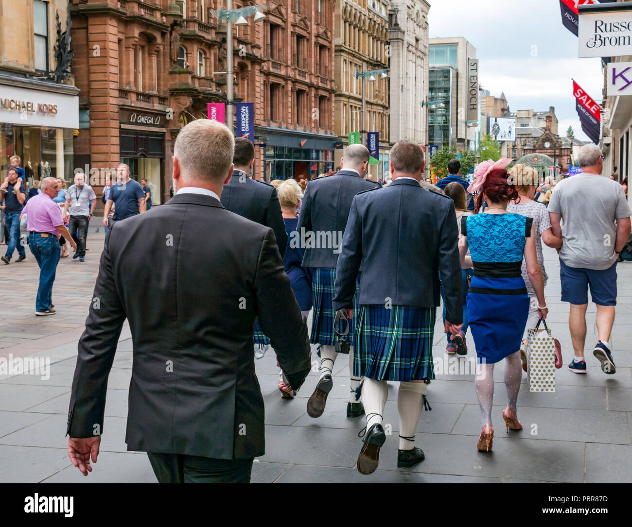 Donna vestita per nozze con uomini in kilts camminando su occupato Buchanan Street, Glasgow, Scotland, Regno Unito Foto Stock