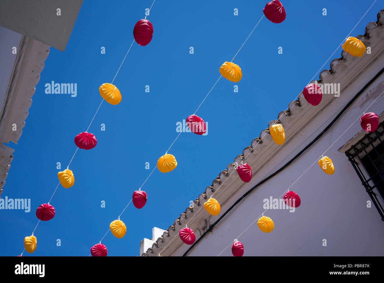 Lanterne di carta appeso sopra una strada con un cielo blu ed edificio dipinto di bianco sullo sfondo Foto Stock