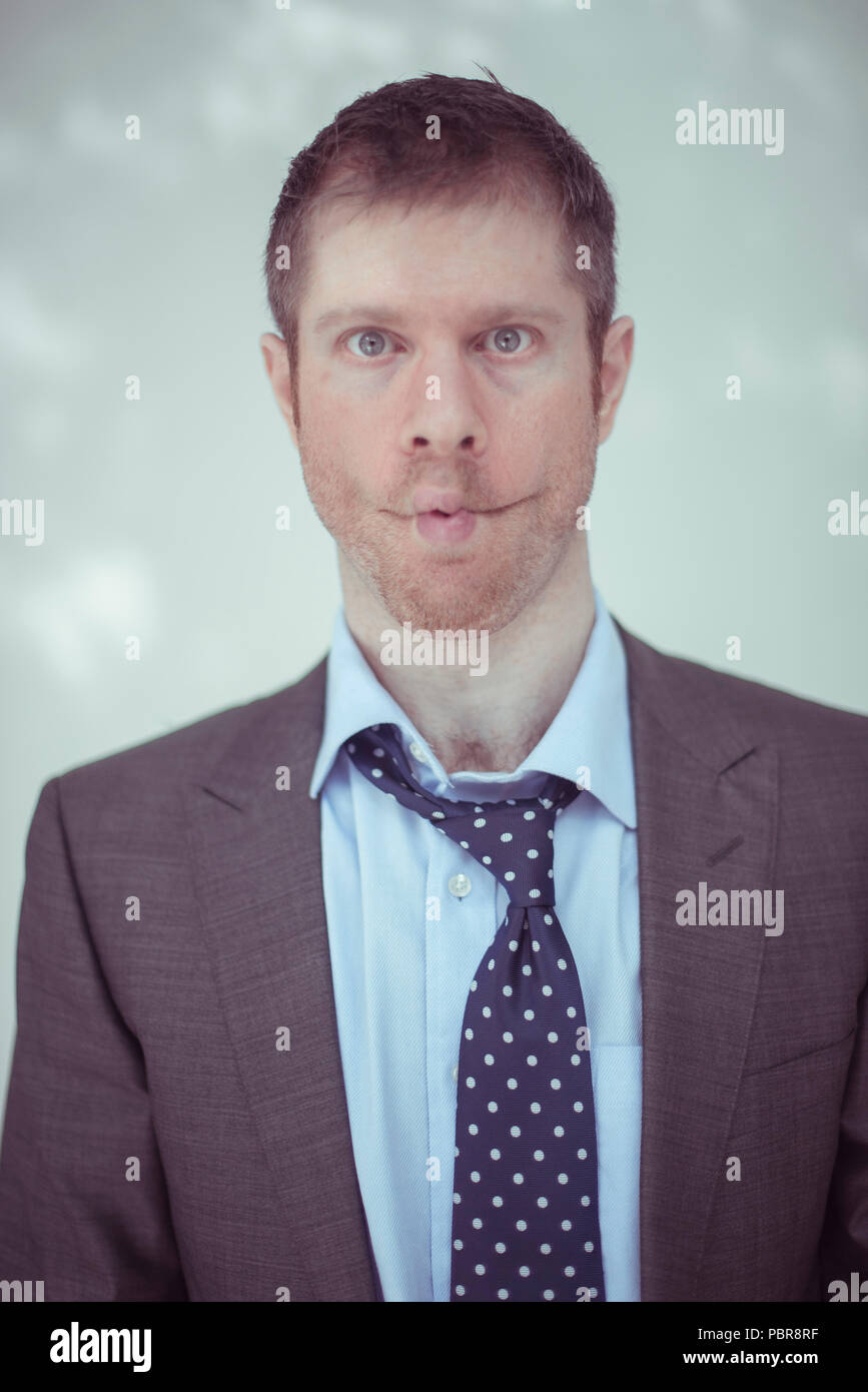Maschio caucasico nella sua 30's indossando un abito grigio, rimosse camicia e cravatta allentata, facendo una faccia di pesce. Foto Stock