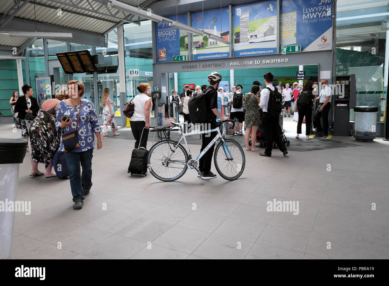 Ciclista con la bici e i passeggeri diretti attraverso la barriera del biglietto dopo essere scesi a Great Western in treno da Londra a Swansea stazione ferroviaria del Galles Foto Stock