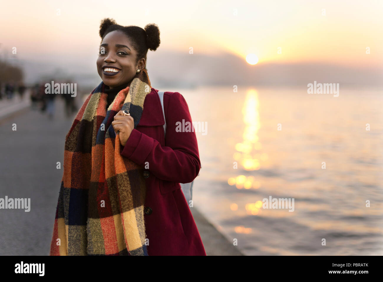 Ritratto di un 25 anni donna africana con un rivestimento di colore rosso e la trama vicino al bordo delle acque con un tramonto. Foto Stock