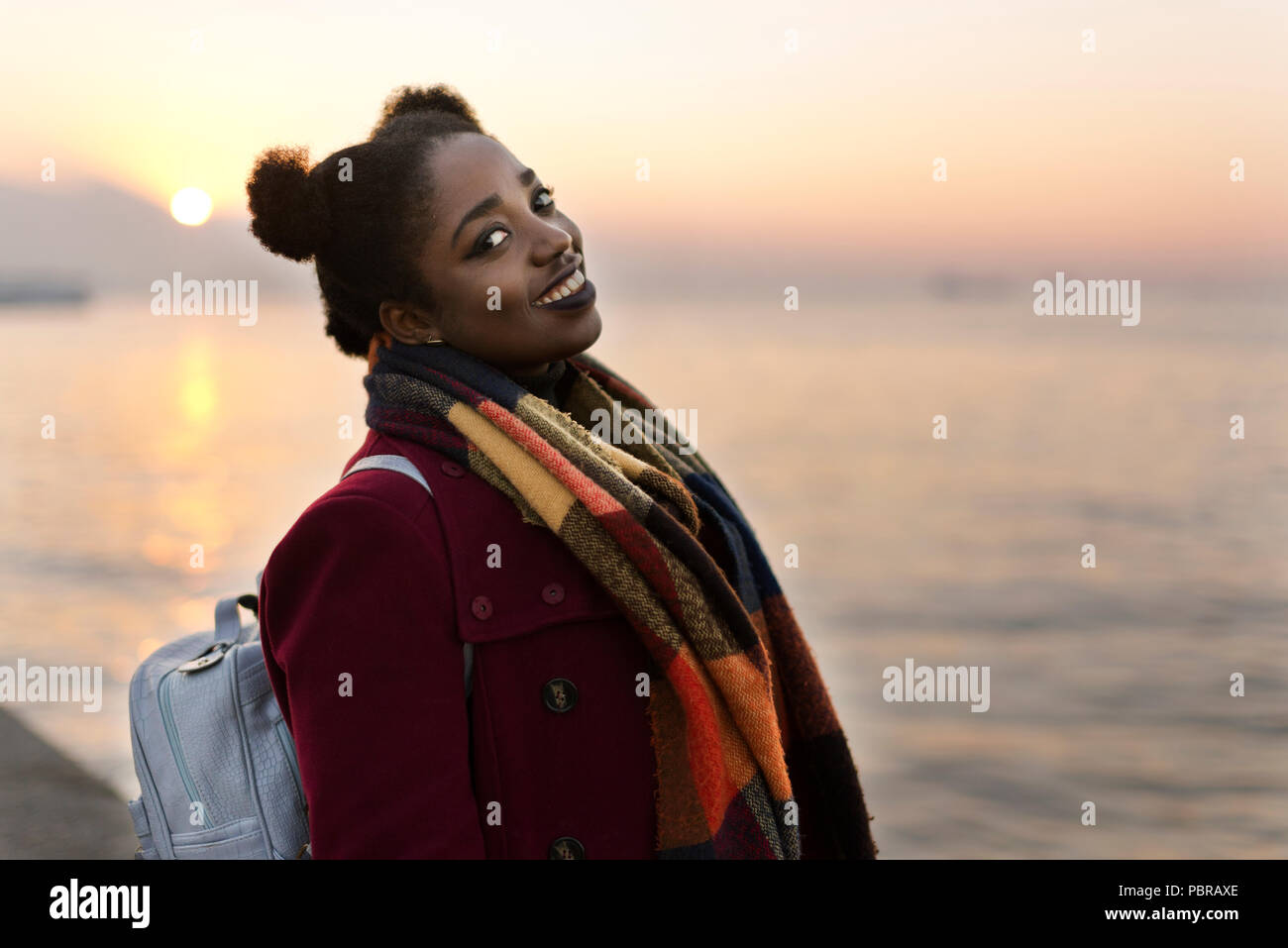 Ritratto di un 25 anni donna africana con un rivestimento di colore rosso e la trama vicino al bordo delle acque con un tramonto. Foto Stock