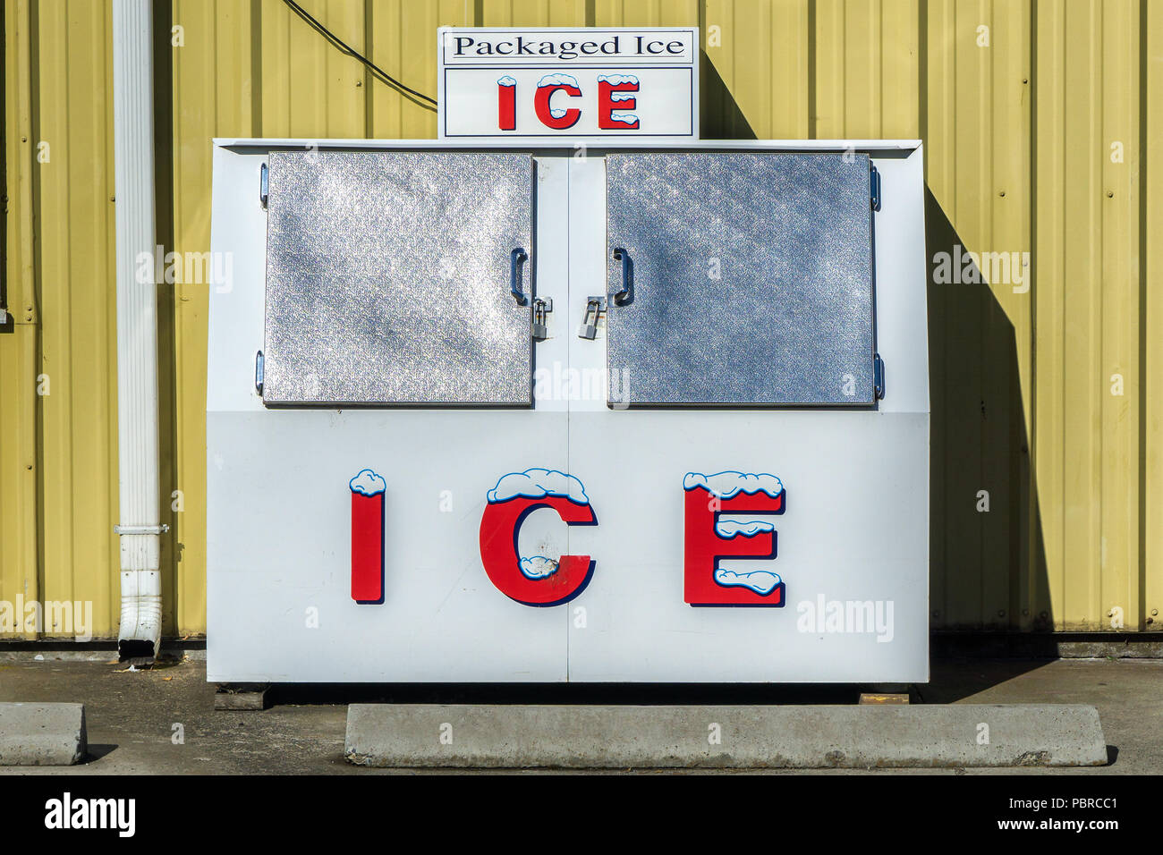 Ghiaccio confezionato congelatore macchina contro una parete gialla durante una calda e soleggiata giornata di estate al di fuori di un negozio di alimentari, Oregon, Stati Uniti d'America. Foto Stock