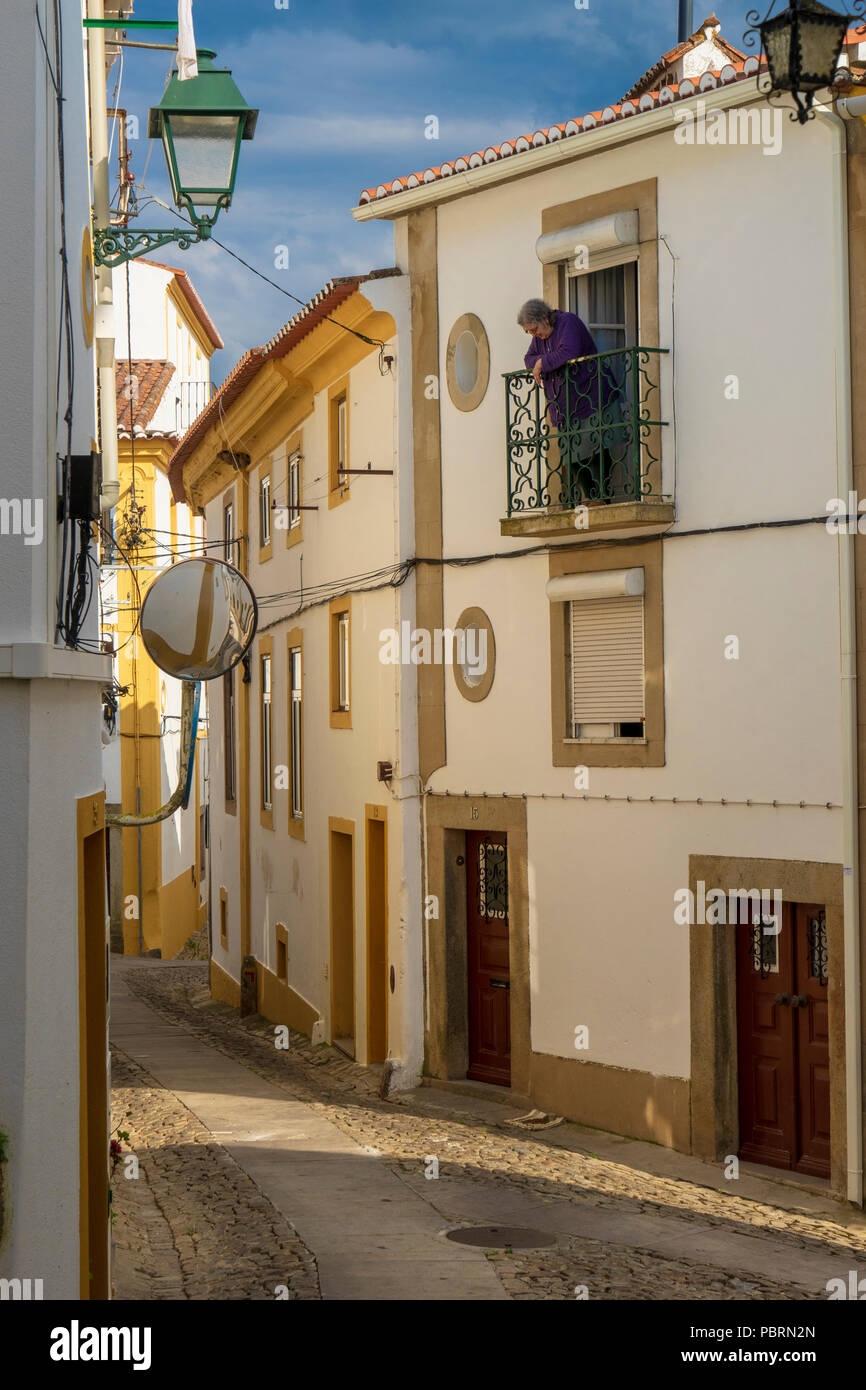 Senior donna appoggiata al suo balcone in ferro che si affaccia le strette strade medievali di Castelo de Vide il Portogallo Foto Stock