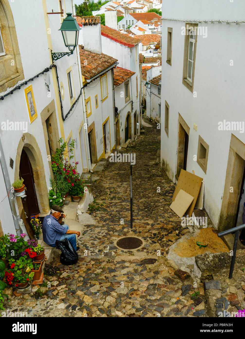 Un uomo anziano seduto sul gradino anteriore di una casa in una strada molto stretta e ripida di Castelo de vide Alentejo Portogallo Foto Stock